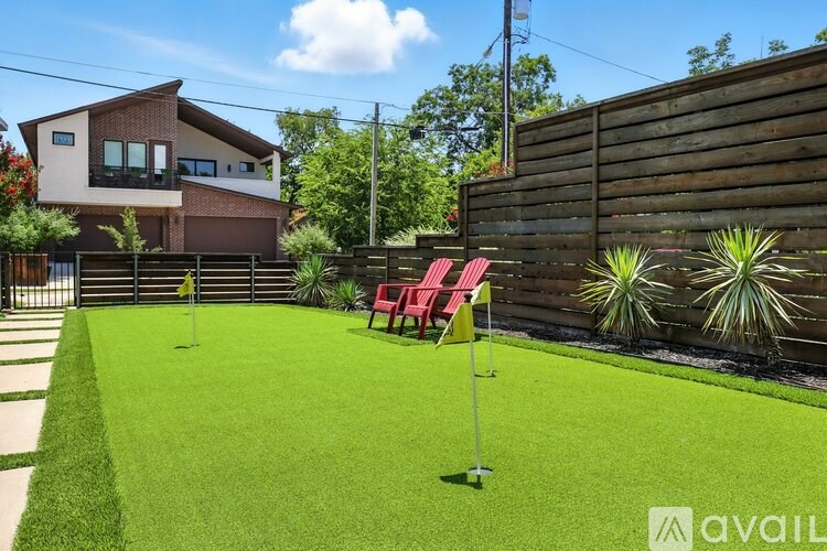 A backyard with a lawn, a small putting green, and a house in the background.