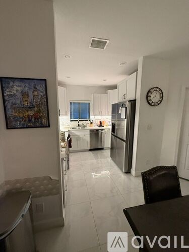 A kitchen with a fridge, a dining table and a painting on the wall.