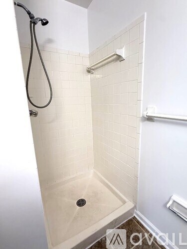 A white tiled shower with a black shower head and hand held shower.