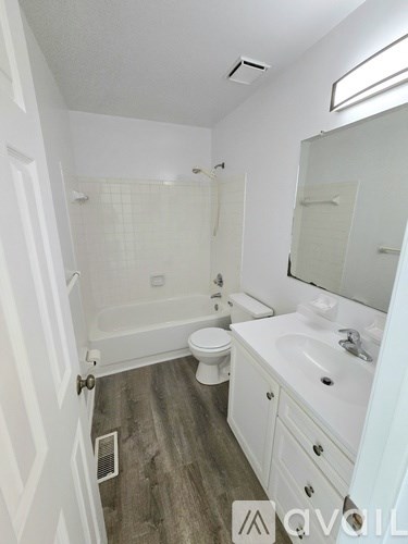 A white bathroom with wood flooring and a white toilet.