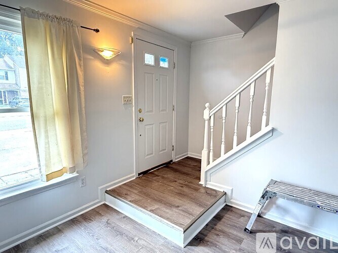 A room with a white door, a window with yellow curtains, and a wooden staircase.