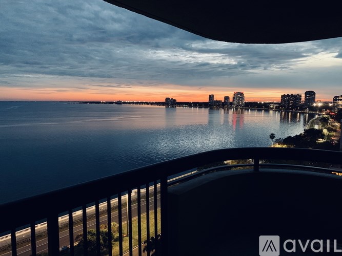 A view from a balcony overlooking a body of water with buildings in the distance during sunset.