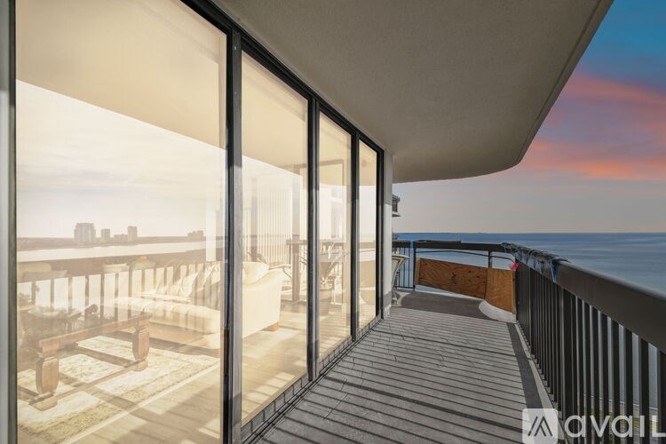 A balcony with glass doors overlooking a city skyline at sunset.