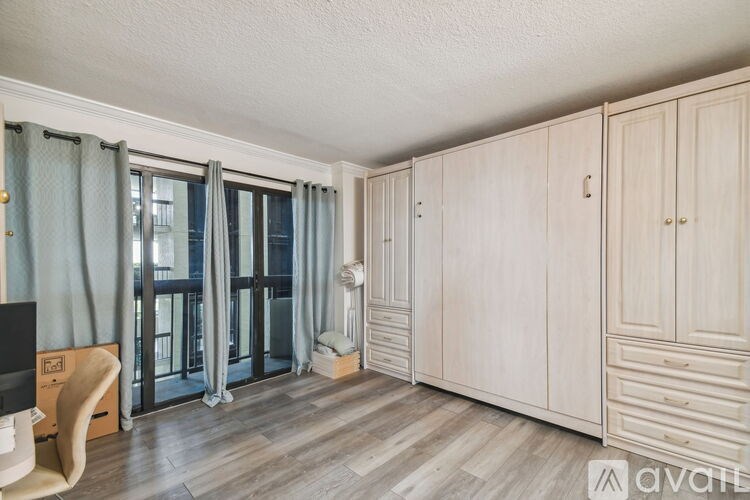 A room with wooden floors and cabinets, a chair, and a balcony with curtains.