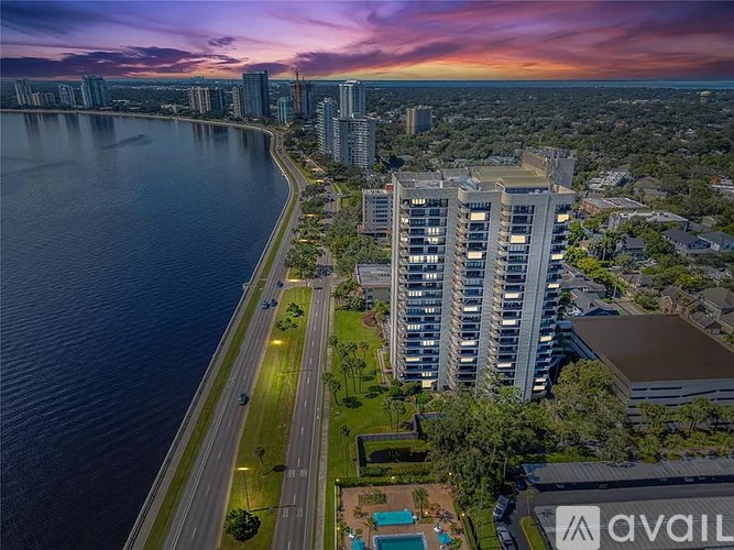A modern building is situated by a body of water with a sunset in the background.