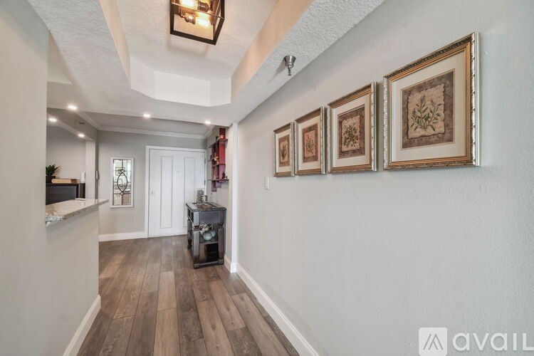 A hallway with a wooden floor and white walls, with a chandelier hanging from the ceiling and pictures on the wall.