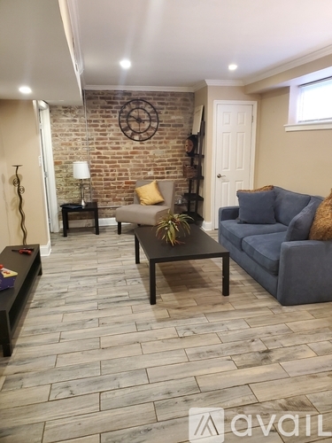 A living room with a grey couch, a black coffee table, and a brick wall.