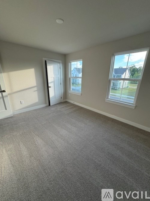 A room with a carpeted floor and a window showing a view of a house.
