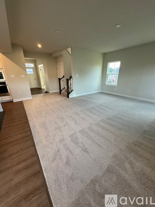 A spacious living room with a carpeted floor and a wooden staircase.