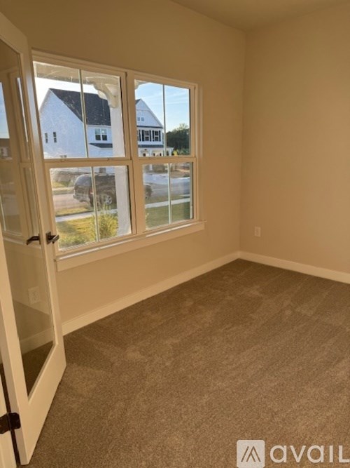 A room with a carpeted floor and a sliding glass door leading to a view of a street and houses.