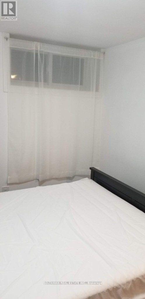 A bed with white bedding in a room with a window covered by sheer curtains.