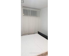 A bed with white bedding in a room with a window covered by sheer curtains.