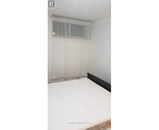 A bed with white bedding in a room with a window covered by sheer curtains.