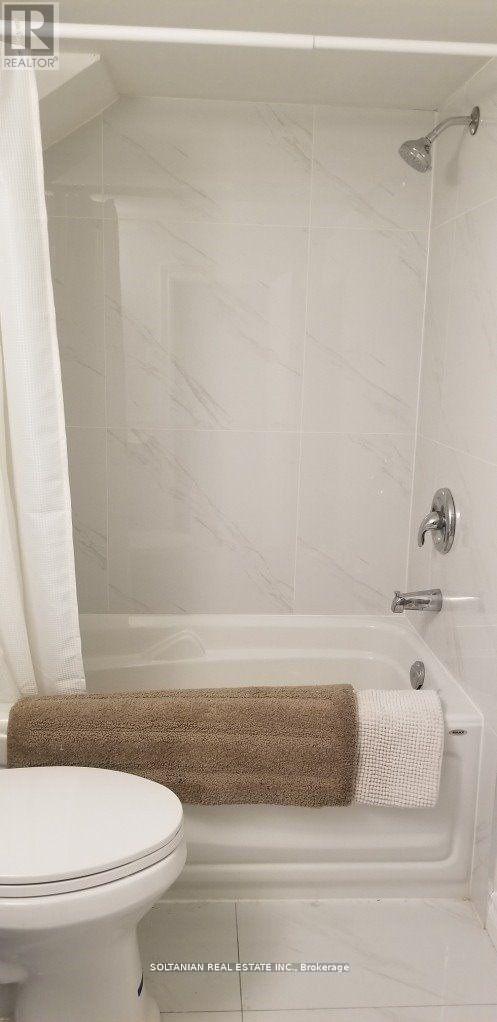 A white toilet sits next to a white bathtub with a brown towel on the side.