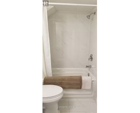 A white toilet sits next to a white bathtub with a brown towel on the side.