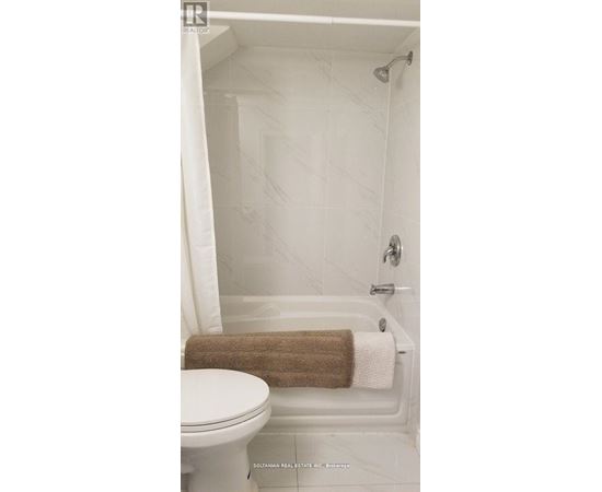 A white toilet sits next to a white bathtub with a brown towel on the side.