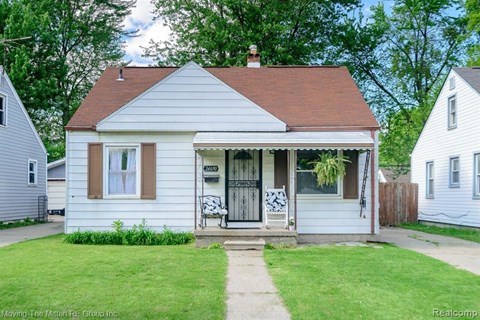 A small white house with a brown roof and a porch.