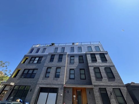 A grey building with a brown door and windows on the second floor.