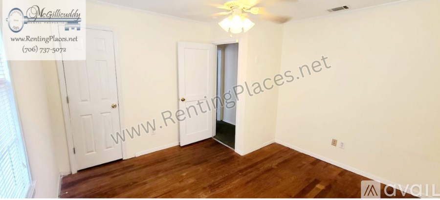 A room with a wooden floor and white walls, with a door on the left and a window on the right.