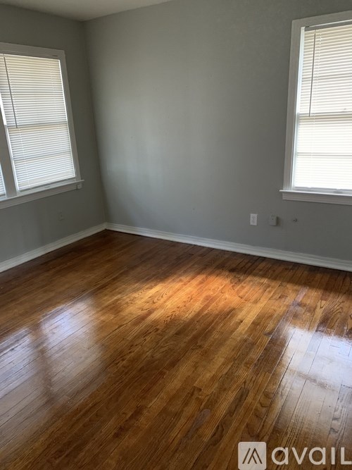 A room with wooden flooring and two windows.