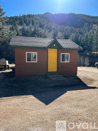 A small brown house with a yellow door stands in front of a mountain.