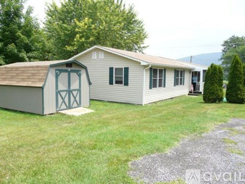 A house with a grey roof and green shutters is surrounded by a grassy lawn and trees.
