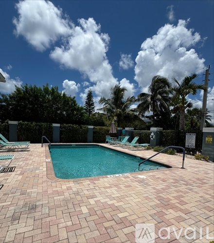 A pool surrounded by a brick patio and palm trees under a blue sky with clouds.