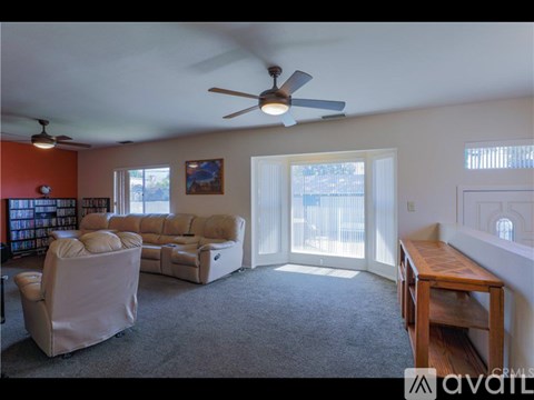 A living room with a grey carpet and a ceiling fan.