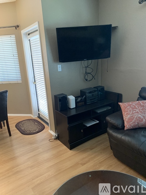 A living room with a black leather couch and a television mounted on the wall.