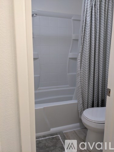 A bathroom with a toilet, a bathtub with a grey shower curtain.