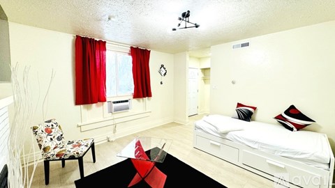 A bedroom with a bed, chair, and window with red curtains.