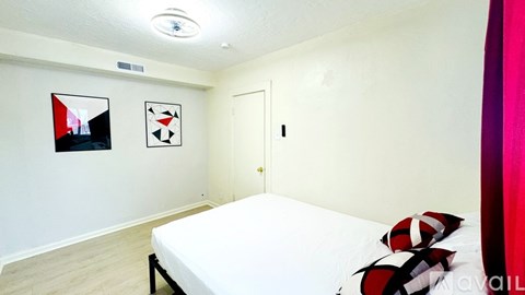 A bedroom with a white bed and two abstract paintings on the wall.
