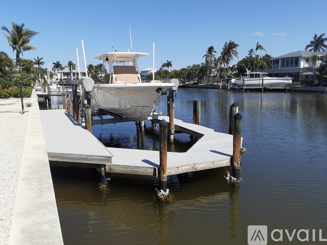 A boat is docked at a pier with a house and palm trees in the background.