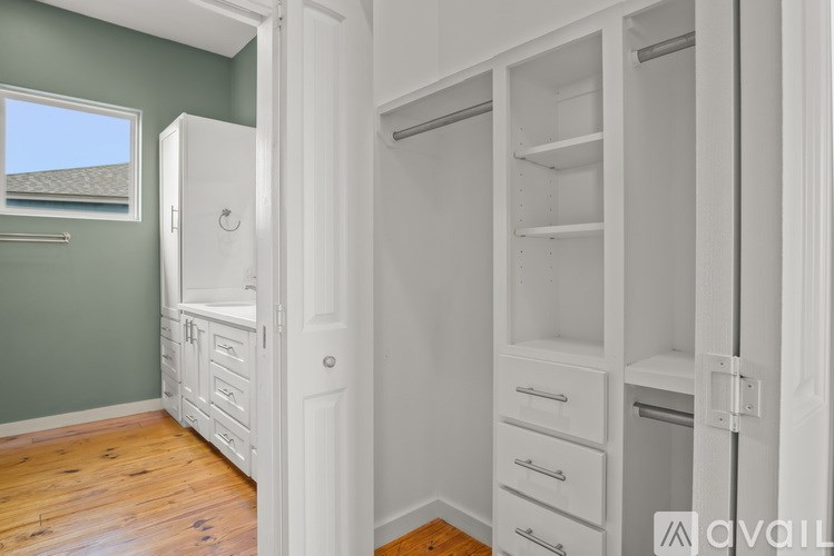 A white closet with drawers and shelves is open to a room with a green wall and a window.