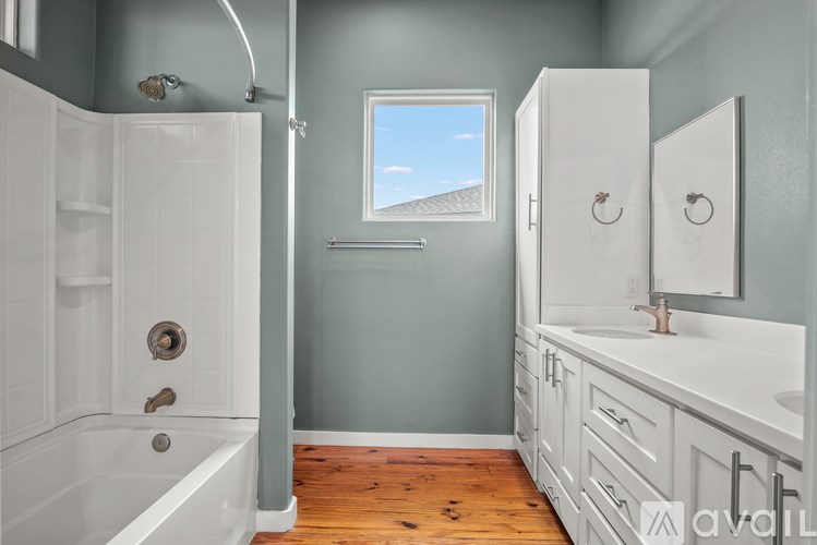 A bathroom with a white tub and sink, a window, and a wooden floor.