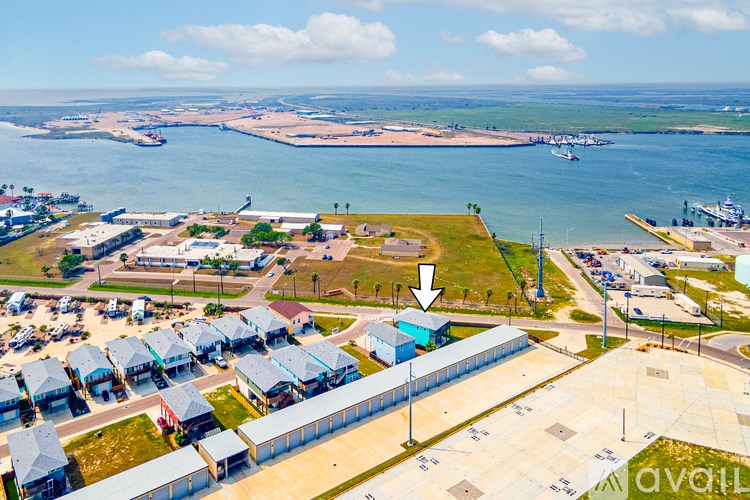 A bird's eye view of a coastal area with a large body of water, boats, and a small town with buildings and a parking lot.