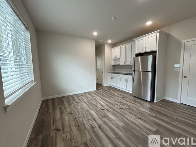 A kitchen with a refrigerator, cabinets, and a wooden floor.