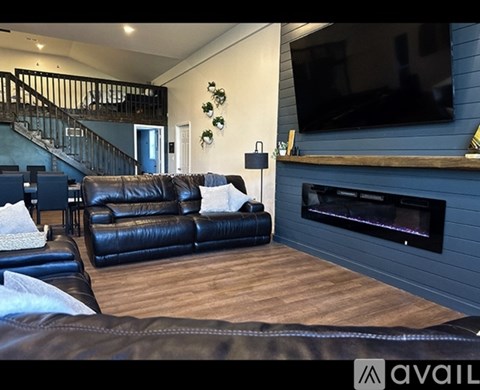 A living room with a black leather couch and a television mounted on the wall.
