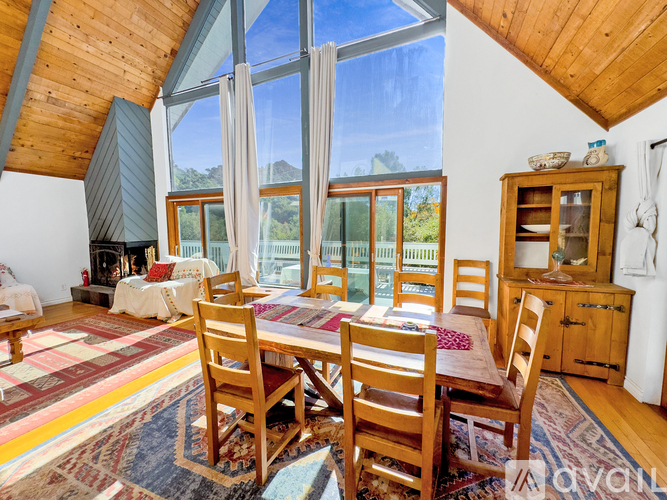 A wooden dining table with chairs is set up in a room with a large window.