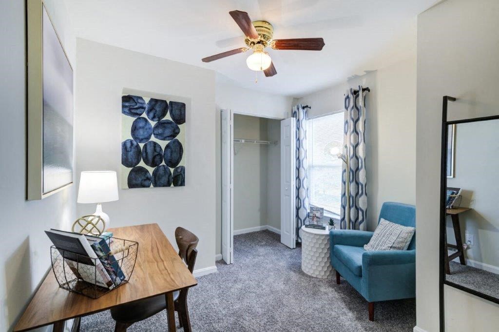 a living room with a desk and a ceiling fan