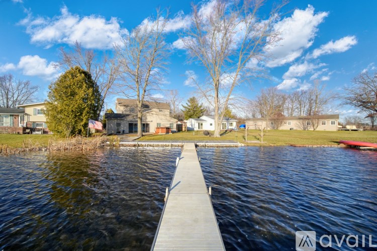 A dock extends into a body of water with houses and trees in the background.
