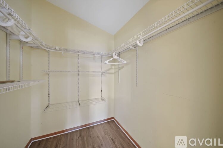 A room with a white ceiling and a wooden floor with a white shelf and clothes hangers.