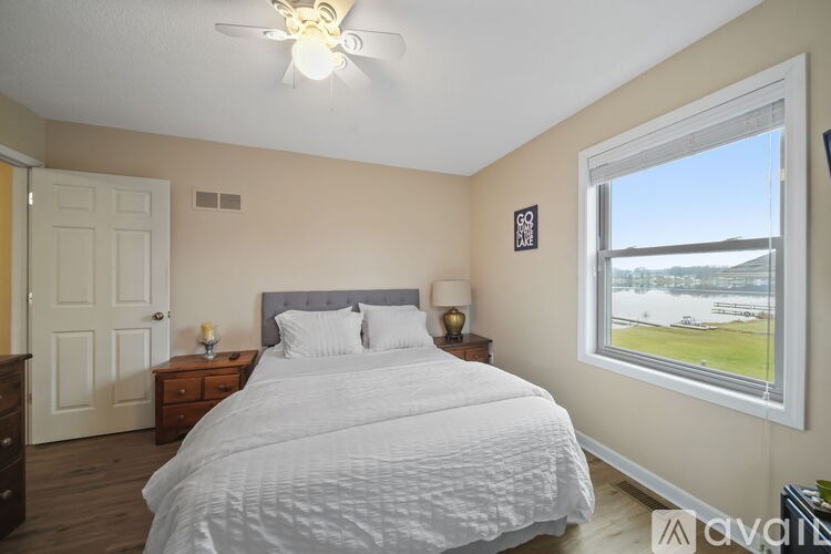A bedroom with a large bed, a ceiling fan, and a window overlooking a field.