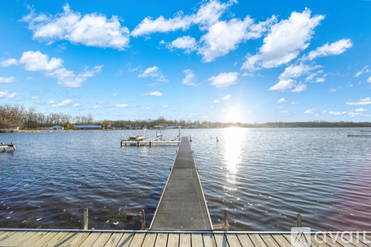 A dock extends into a calm body of water under a blue sky with scattered clouds.
