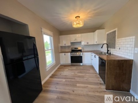A kitchen with a black fridge, wooden floors, and white cabinets.