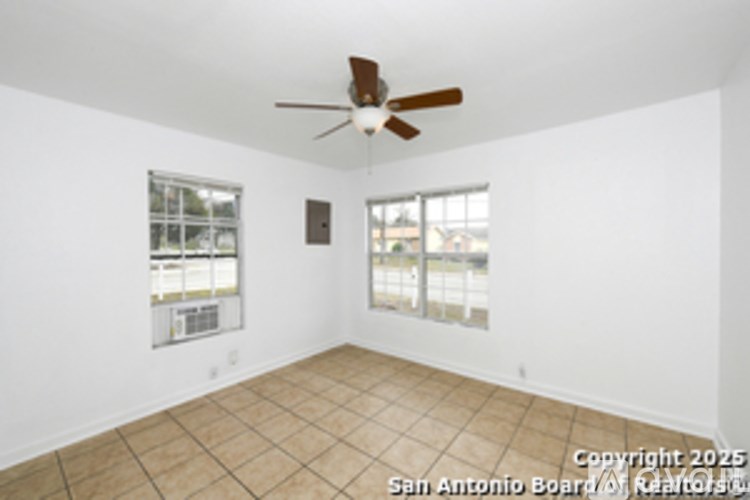 Empty room with a ceiling fan and two windows.