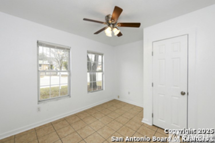 A room with a ceiling fan and two windows.