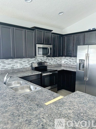 A kitchen with black cabinets and a stainless steel refrigerator.