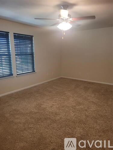 A room with a carpeted floor, a ceiling fan, and a window with blinds.