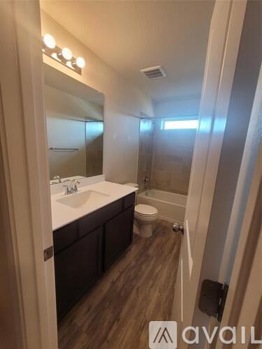 A bathroom with a sink, mirror, toilet and wooden floors.